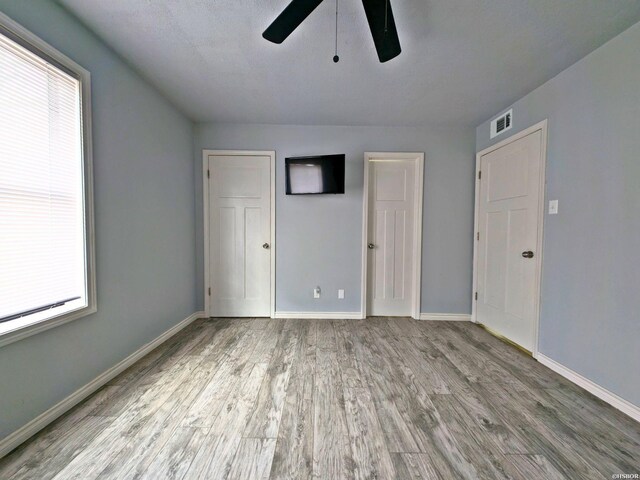 unfurnished bedroom with light wood-type flooring, visible vents, baseboards, and multiple windows