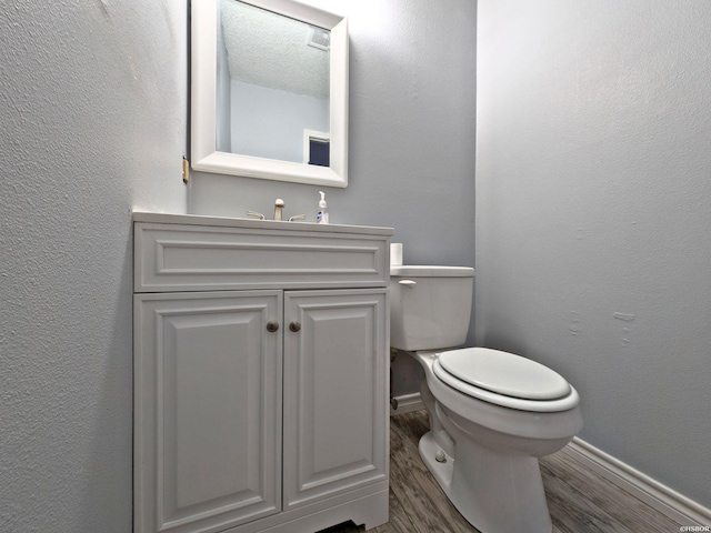 bathroom featuring a textured wall, toilet, vanity, wood finished floors, and baseboards