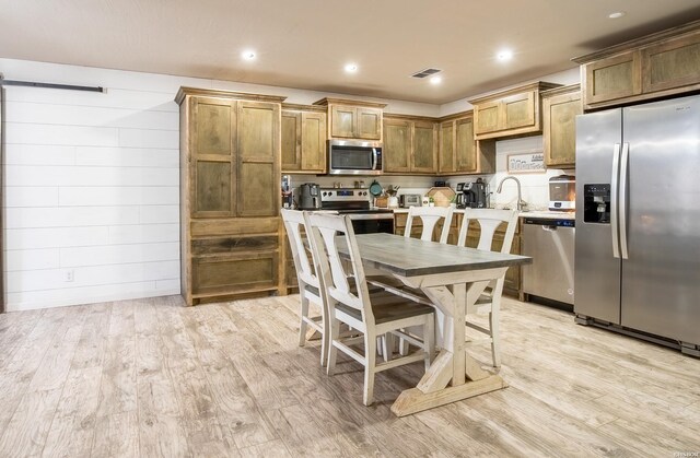 kitchen with light wood finished floors, brown cabinetry, appliances with stainless steel finishes, a kitchen breakfast bar, and light countertops