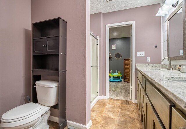 full bathroom featuring double vanity, toilet, a sink, a textured ceiling, and baseboards