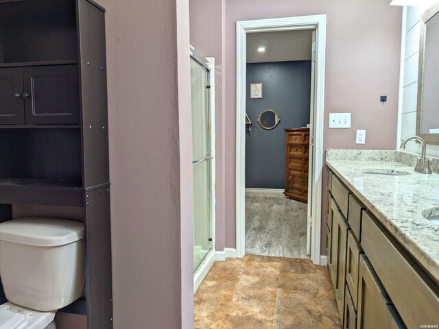 bathroom featuring double vanity, a stall shower, baseboards, toilet, and a sink