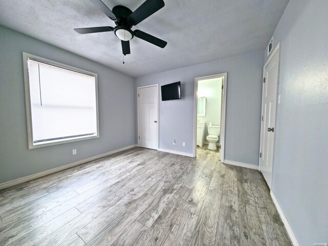 unfurnished bedroom with a textured ceiling, ensuite bathroom, visible vents, baseboards, and light wood-style floors