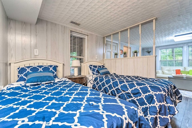 bedroom with wooden walls, wood finished floors, crown molding, and visible vents