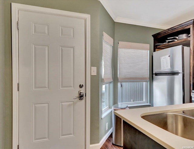 kitchen with baseboards, ornamental molding, freestanding refrigerator, light countertops, and a sink