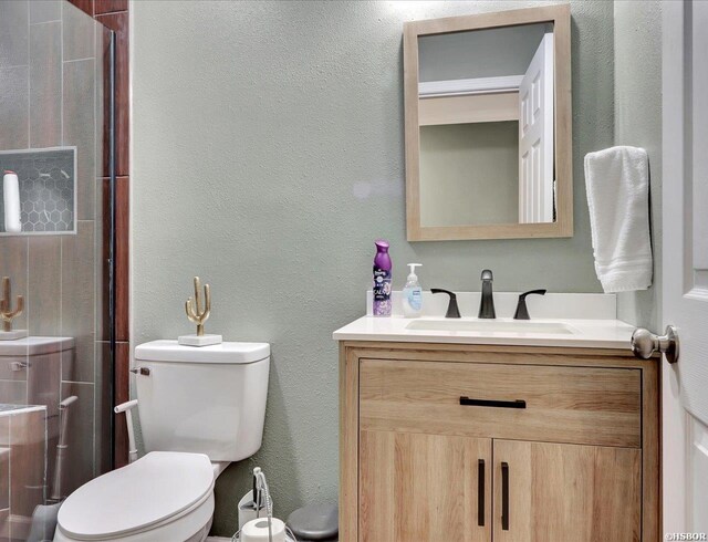 full bathroom with a textured wall, a shower with shower door, vanity, and toilet