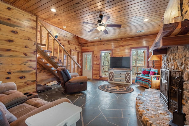 living area with wooden ceiling, stairs, wooden walls, and a stone fireplace