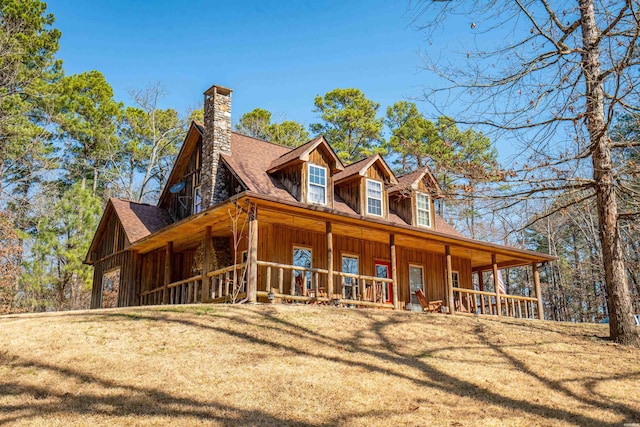 view of property exterior with covered porch, roof with shingles, a lawn, board and batten siding, and a chimney