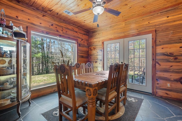 dining area featuring stone tile flooring, wooden ceiling, wood walls, and french doors