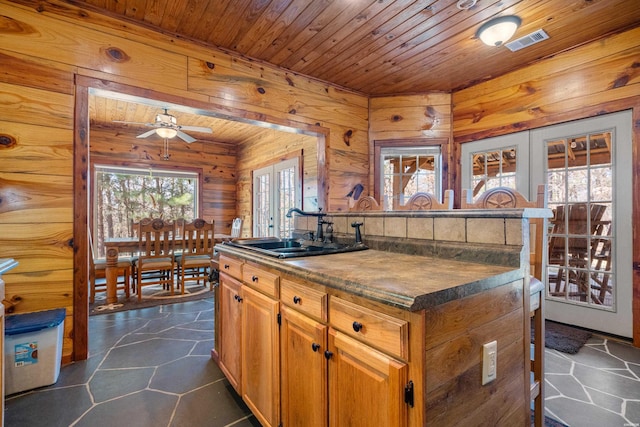 kitchen with wood walls, wooden ceiling, a sink, and visible vents