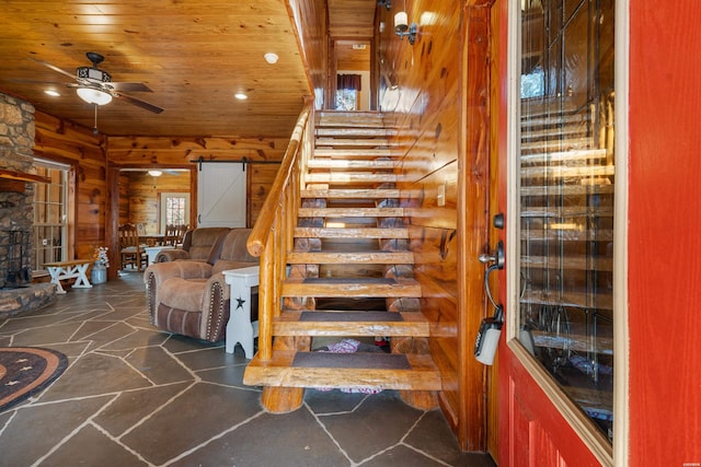 staircase featuring a barn door, a ceiling fan, wooden ceiling, stone flooring, and wood walls