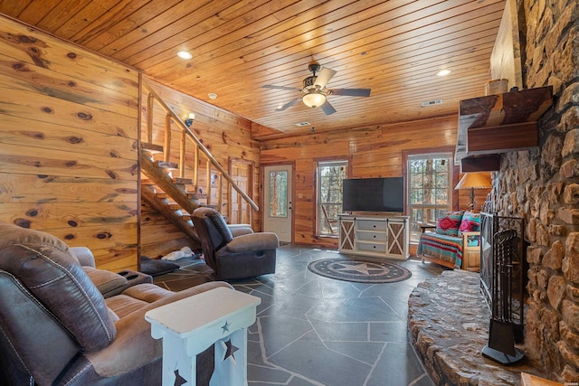 living room featuring a fireplace, stairway, wood ceiling, ceiling fan, and wooden walls