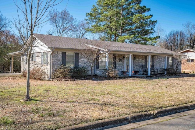 single story home featuring brick siding, roof with shingles, covered porch, and a front yard