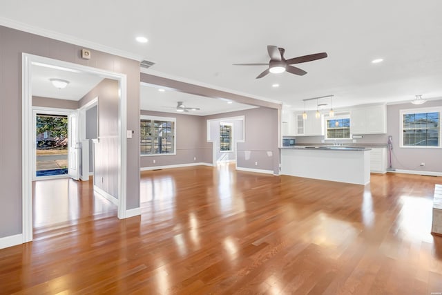 unfurnished living room with light wood-style floors, a healthy amount of sunlight, visible vents, and ornamental molding