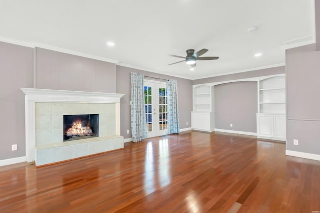 unfurnished living room with built in features, a tile fireplace, ornamental molding, wood finished floors, and french doors