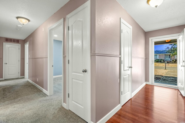 hallway with a textured ceiling, carpet floors, a wainscoted wall, and visible vents