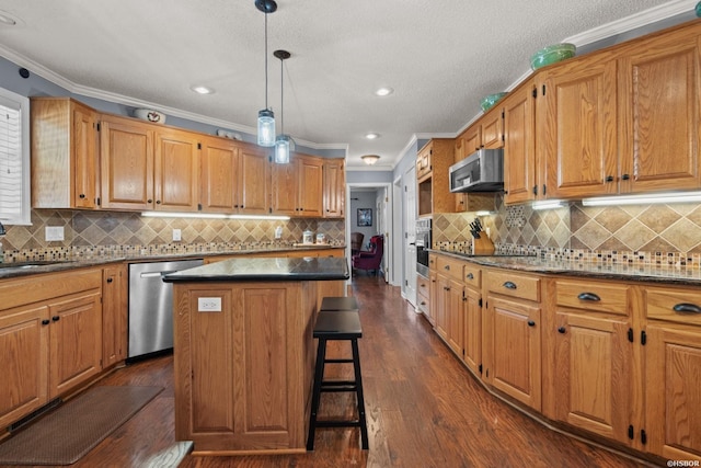 kitchen with dark wood-type flooring, a kitchen island, appliances with stainless steel finishes, a kitchen bar, and crown molding