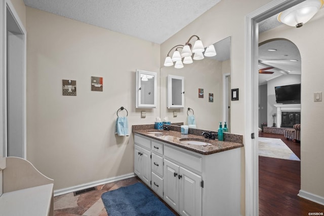 bathroom featuring a textured ceiling, vaulted ceiling, a sink, and a glass covered fireplace