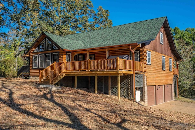 back of property featuring a deck, an attached garage, a shingled roof, concrete driveway, and log exterior