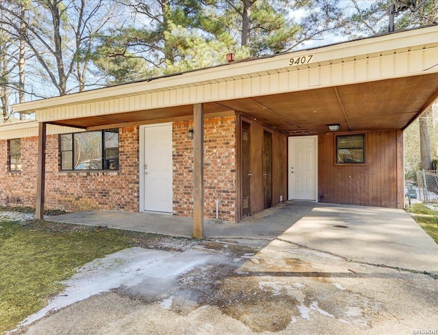 doorway to property with a carport, brick siding, and driveway