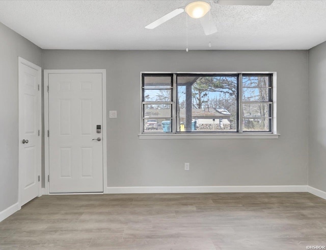 entryway with light wood-type flooring, a ceiling fan, baseboards, and a textured ceiling