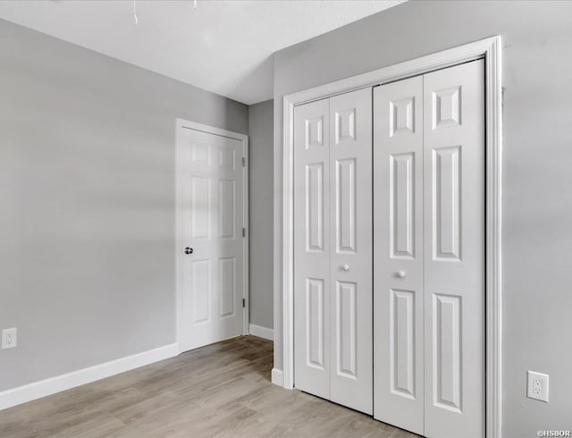 unfurnished bedroom featuring light wood finished floors, a closet, and baseboards