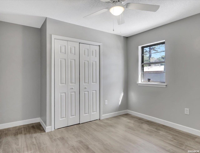 unfurnished bedroom featuring light wood-style floors, a textured ceiling, baseboards, and a closet