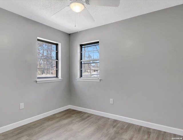 empty room featuring a ceiling fan, light wood-type flooring, a textured ceiling, and baseboards