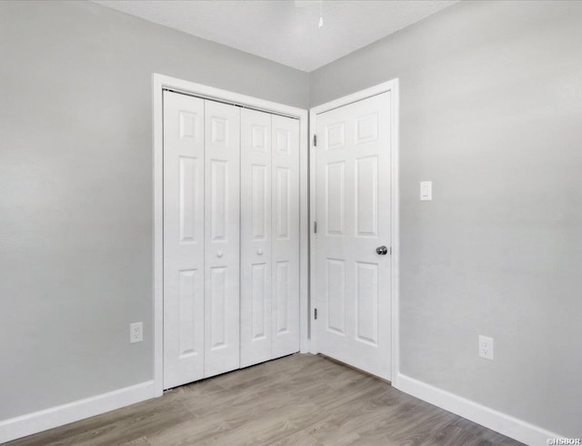 unfurnished bedroom featuring light wood-style floors, baseboards, and a closet