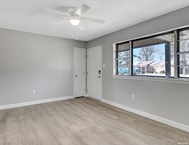 empty room with a textured ceiling, ceiling fan, light wood finished floors, and baseboards