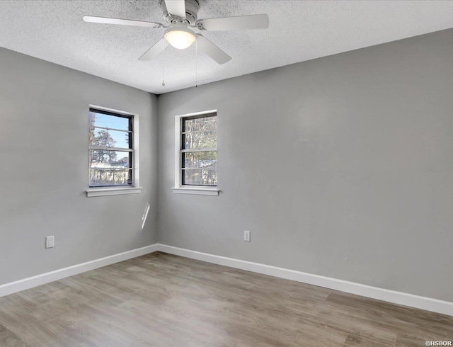 spare room featuring a textured ceiling, light wood finished floors, and baseboards