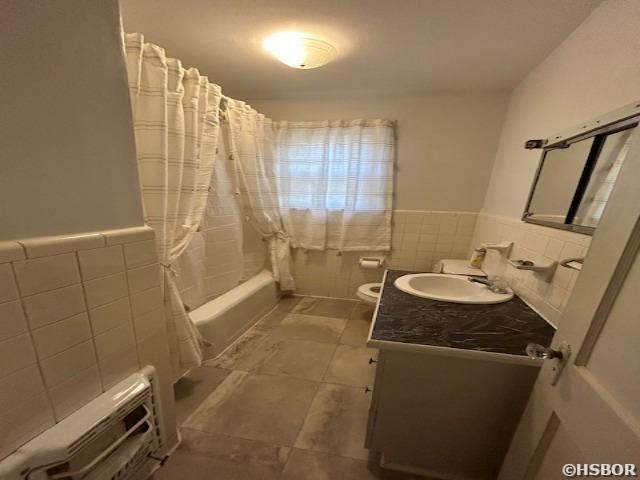 bathroom with toilet, a wainscoted wall, vanity, tile walls, and shower / bathtub combination with curtain