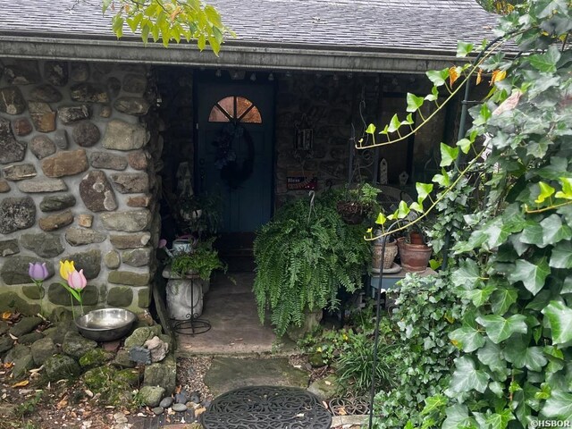 entrance to property with stone siding and roof with shingles