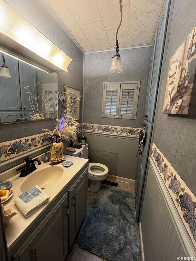 half bath featuring a wainscoted wall, crown molding, vanity, and toilet