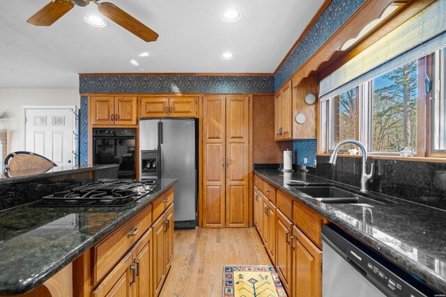 kitchen with light wood-style flooring, brown cabinets, dark stone countertops, black appliances, and a sink