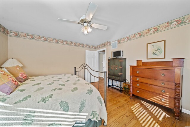 bedroom with a ceiling fan, visible vents, and wood finished floors