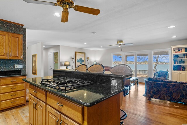 kitchen with light wood finished floors, brown cabinetry, dark stone counters, a kitchen island, and black gas stovetop