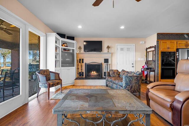 living room with a ceiling fan, light wood-style floors, and a fireplace