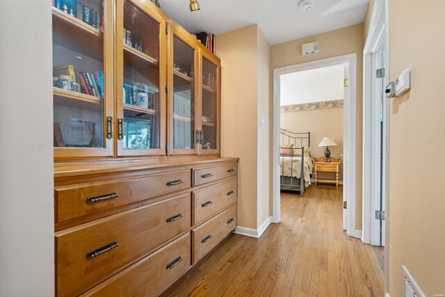 hall featuring light wood-type flooring, visible vents, and baseboards