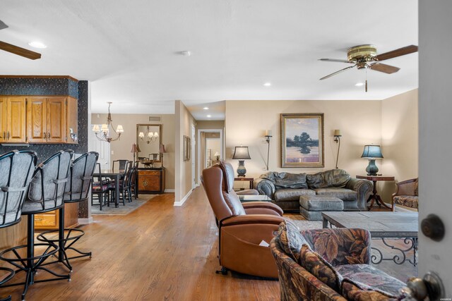 living room with ceiling fan with notable chandelier, light wood finished floors, baseboards, and recessed lighting