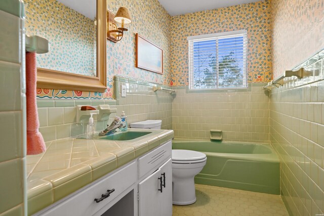 full bathroom with wallpapered walls, wainscoting, tile patterned flooring, vanity, and tile walls