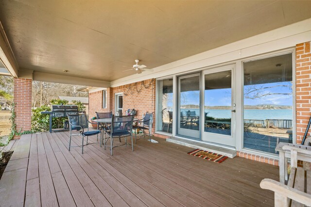 deck featuring area for grilling, outdoor dining area, a water view, and a ceiling fan