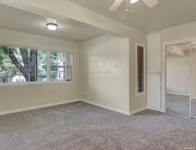 carpeted spare room featuring ceiling fan and baseboards