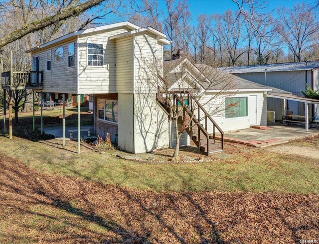 rear view of house featuring a carport, stairs, a chimney, and a lawn