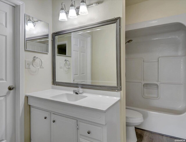 full bath with toilet, washtub / shower combination, wood finished floors, and vanity