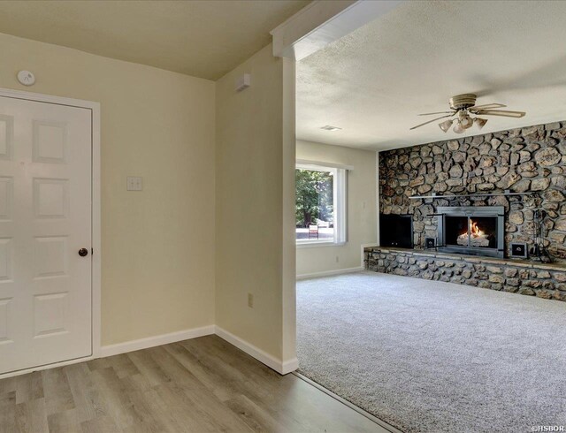 unfurnished living room featuring light wood-style floors, baseboards, a textured ceiling, and a stone fireplace