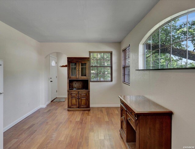 interior space featuring light wood-type flooring, arched walkways, and baseboards