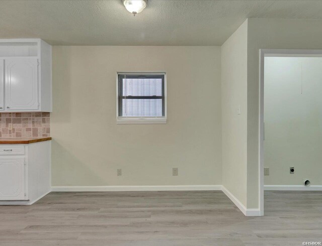 unfurnished dining area with light wood finished floors, baseboards, and a textured ceiling