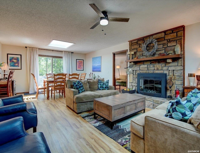 living room featuring a textured ceiling, ceiling fan, a stone fireplace, and wood finished floors