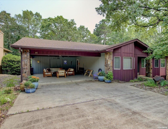 view of front facade with driveway, stone siding, an outdoor living space, and board and batten siding