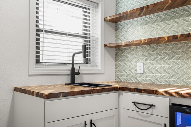 kitchen with a textured wall, butcher block countertops, white cabinetry, open shelves, and a sink